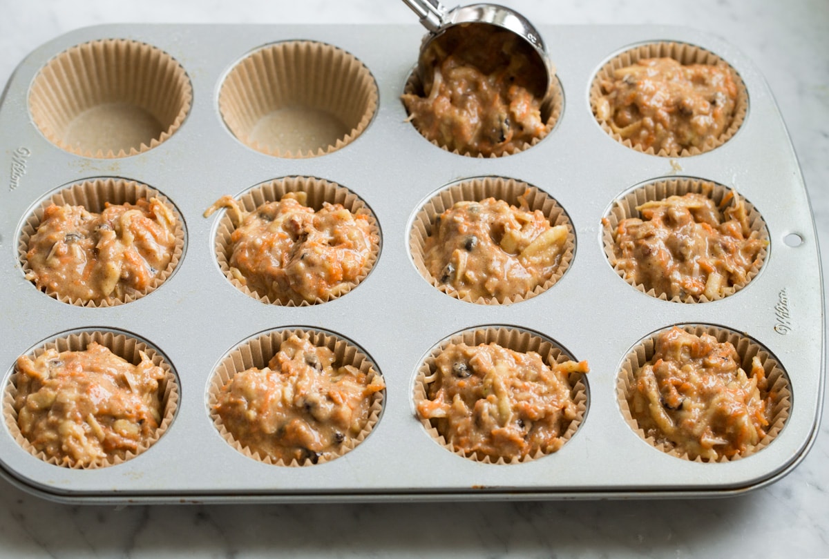 Scooping morning glory muffin batter into a paper lined muffin pan.