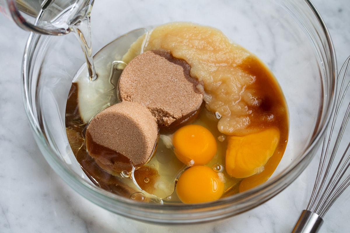 Showing how to make morning glory muffins. Mixing eggs, oil, applesauce, brown sugar and vanilla in a glass mixing bowl.