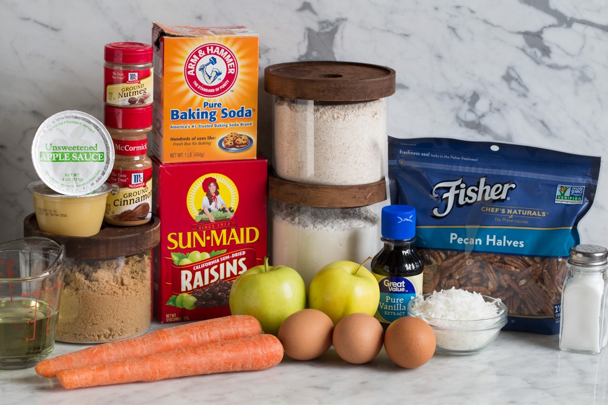 Ingredients needed for morning glory muffins shown here including wheat flour, white flour, baking soda, cinnamon, nutmeg, salt, brown sugar, apples carrots, raisins, coconut, eggs, vegetable oil, vanilla, pecans and applesauce.