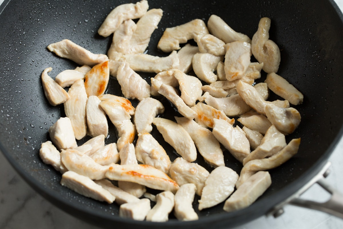 Showing how to make pad thai. Sautéing chicken breasts pieces in a wok.