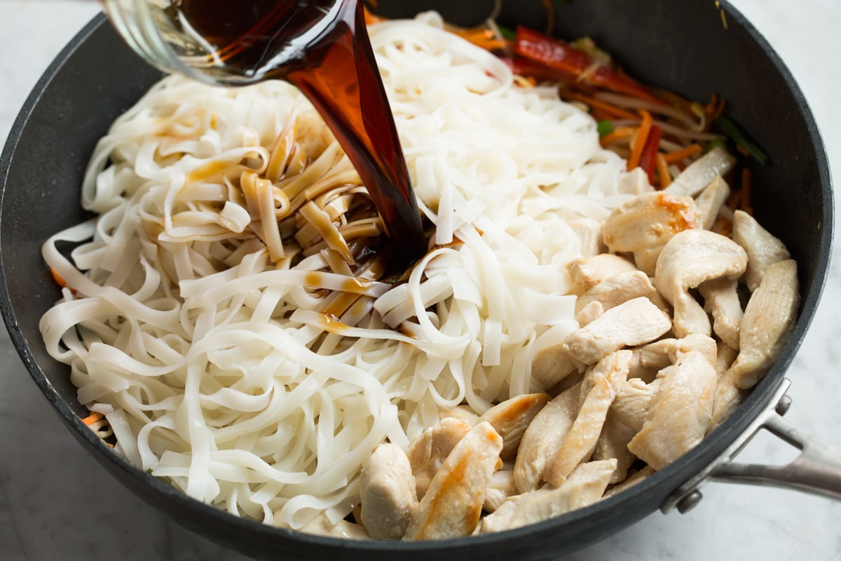 Adding rice noodles, cooked chicken and sauce to finish Pad Thai in wok.