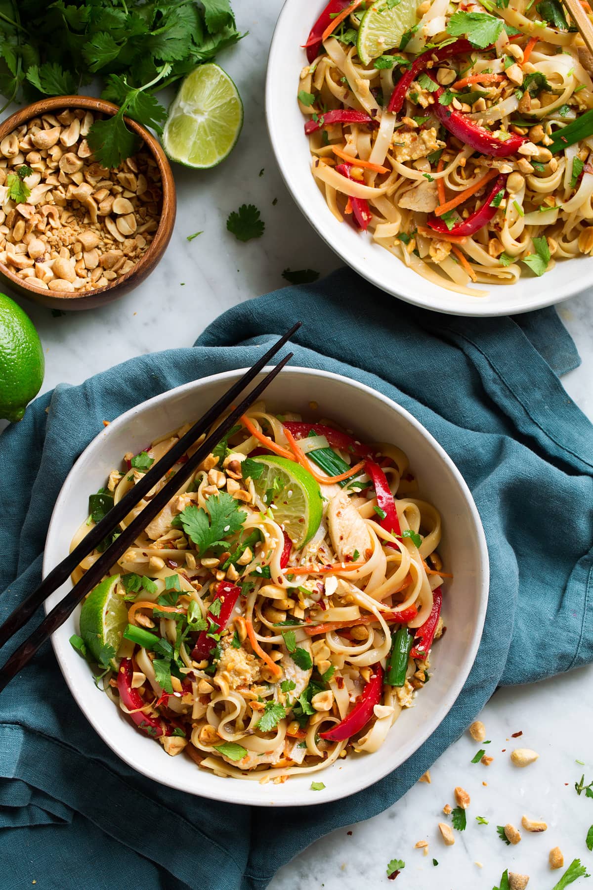 Two servings of pad thai in white bowls, with chopsticks on the side, set over a blue napkin.
