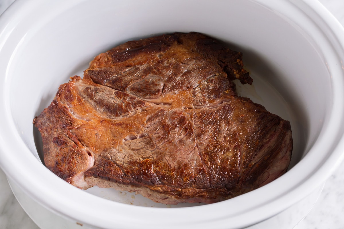 Ultimate Slow Cooker Pot Roast Showing how to make crockpot pot roast, placing seared chuck roast in a slow cooker.