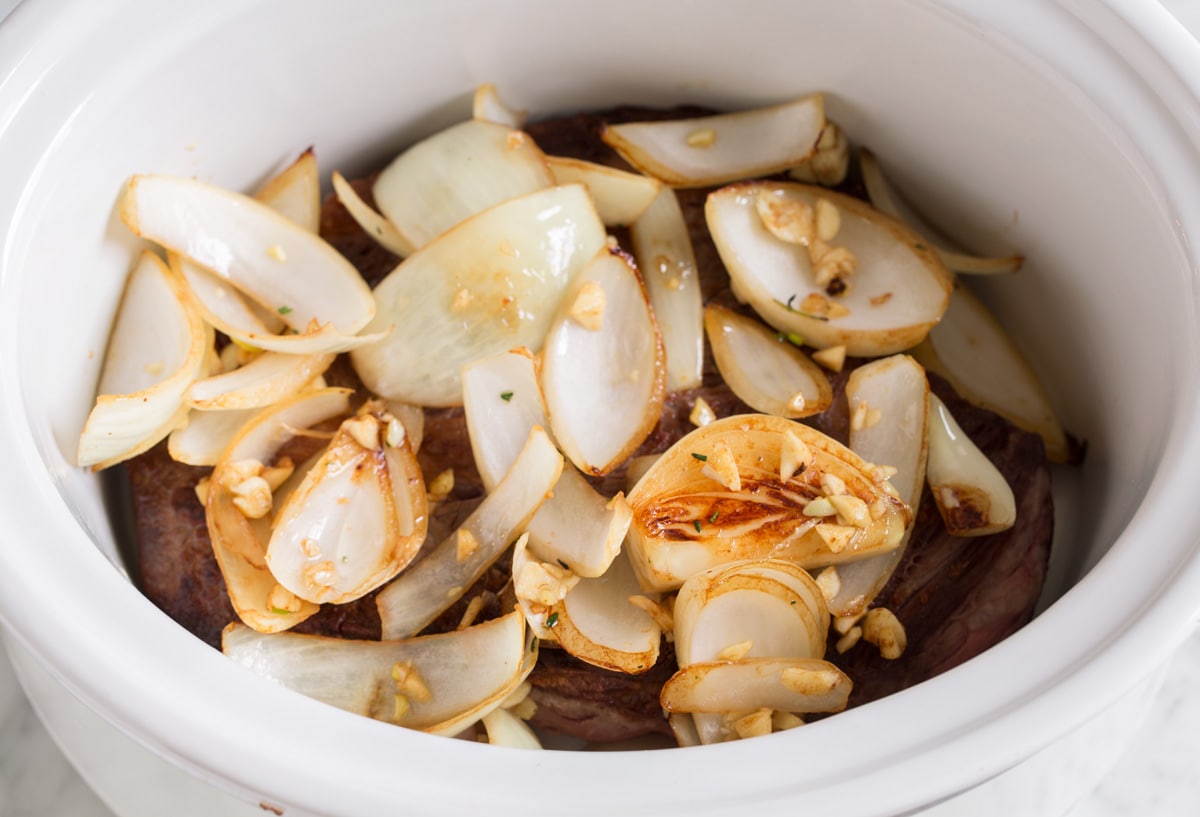 Best Crock Pot Roast Adding sautéed onions and garlic over chuck roast in slow cooker.