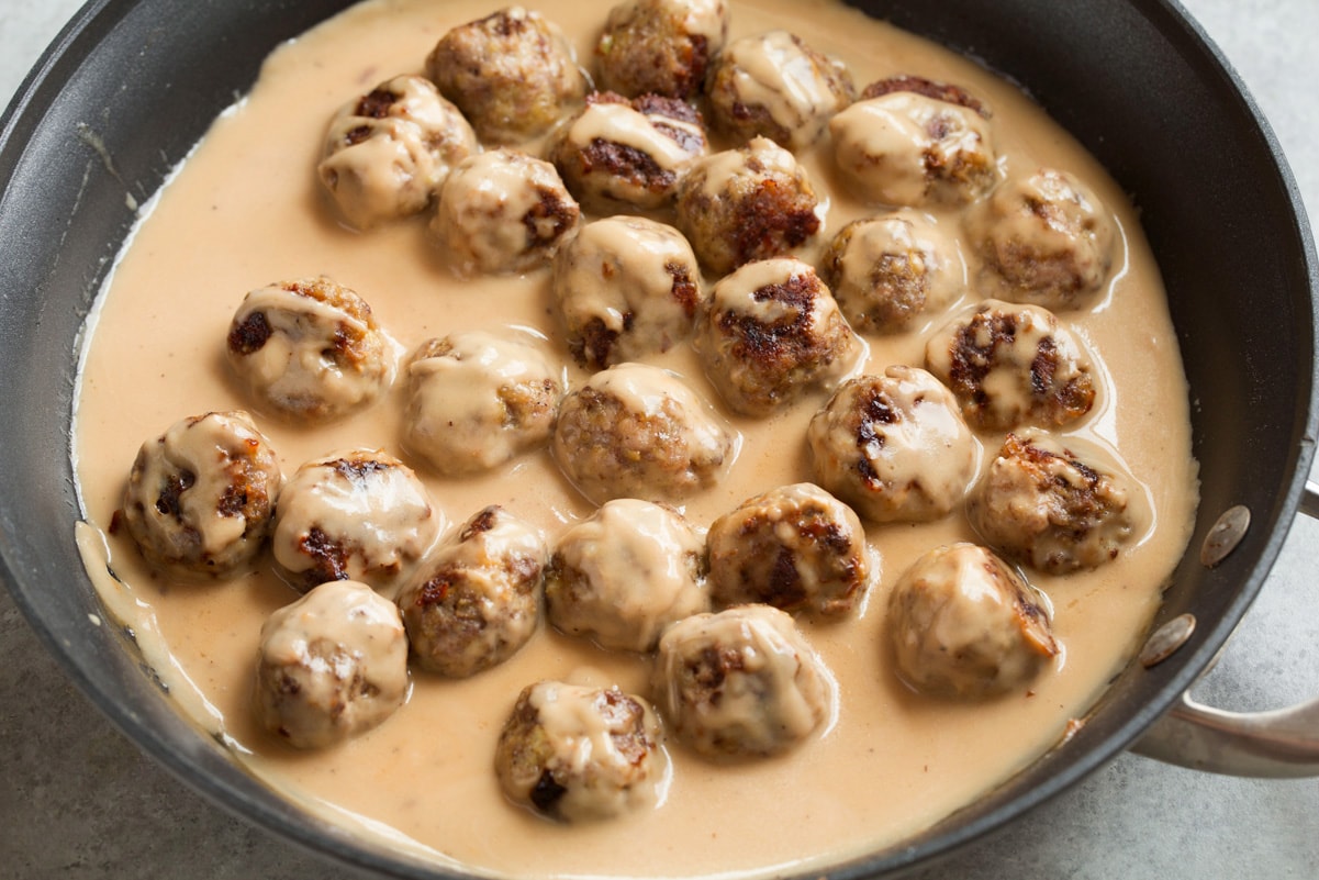 Tossing baked Swedish meatballs with sauce in skillet.