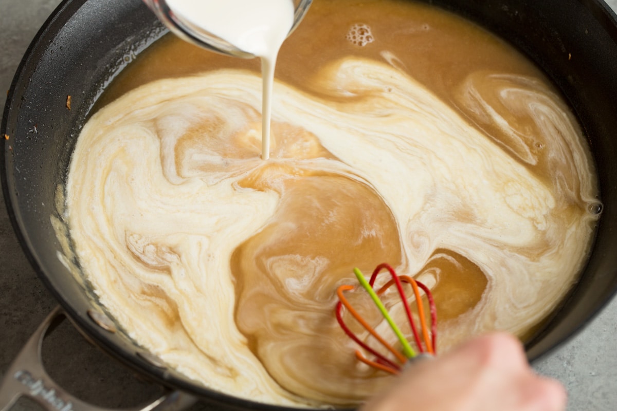 Adding beef broth and cream to skillet to make Swedish meatball gravy.
