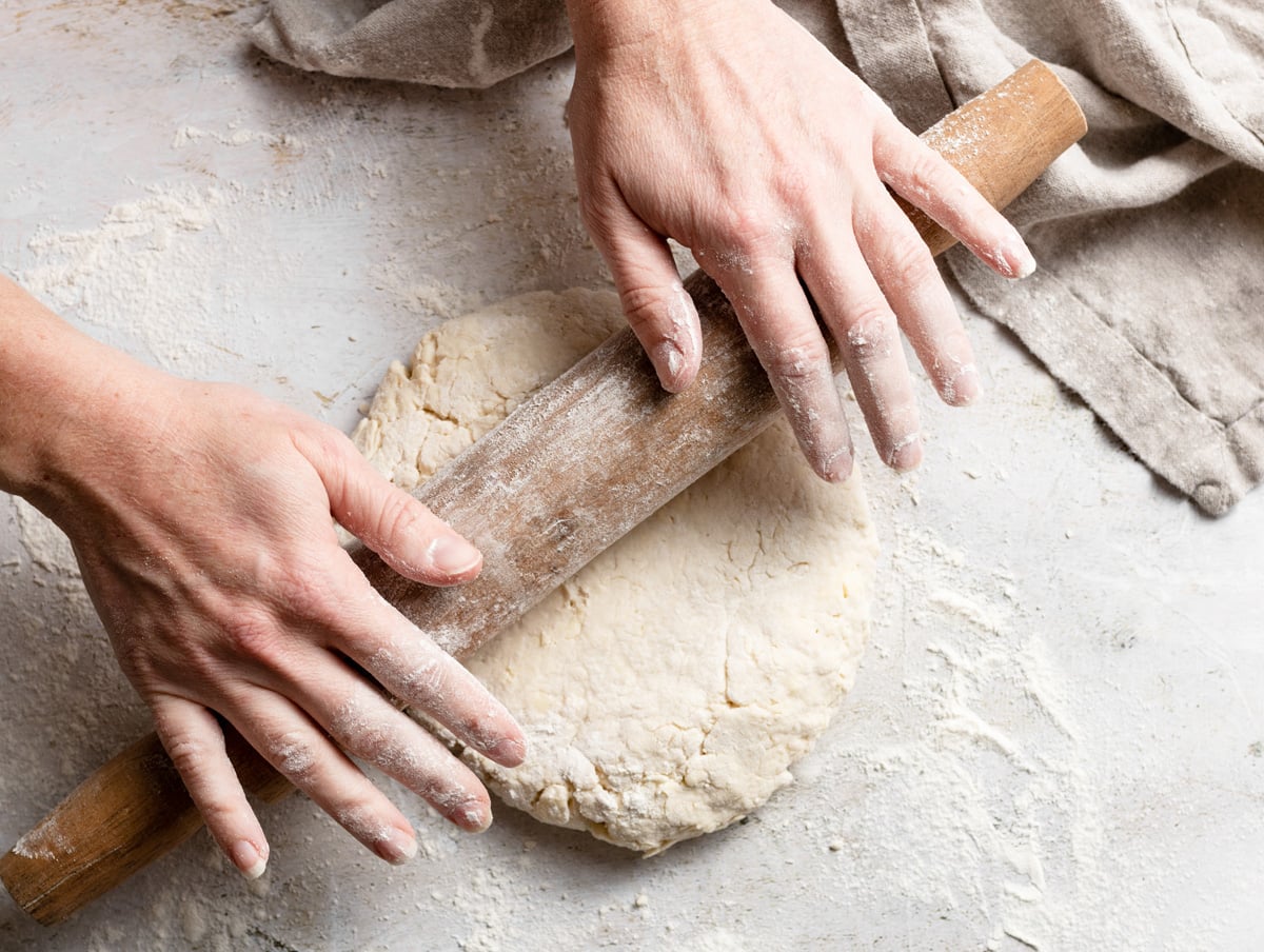 Gently rolling biscuit dough out using a rolling pin on a floured surface.
