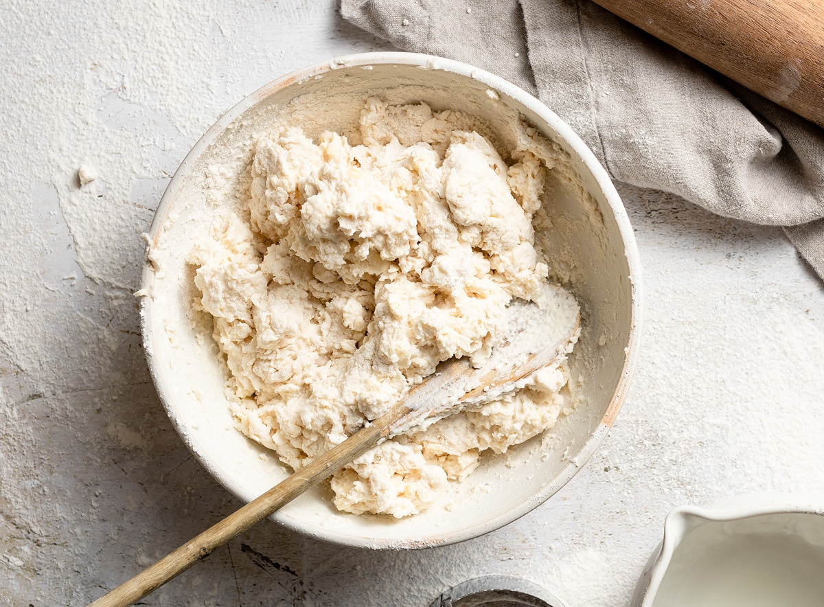 Mixing buttermilk into biscuit dough in a mixing bowl.