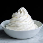 Piped mound of whipped cream in a white bowl set over a marble surface with a black background.