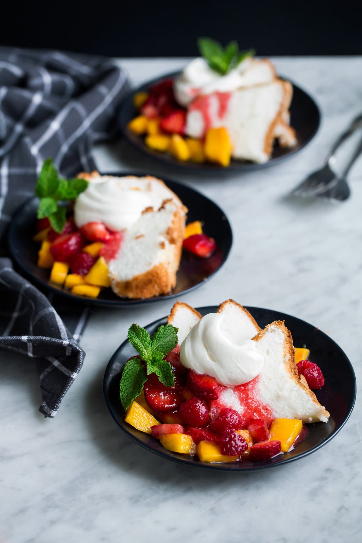 Homemade whipped cream served over angel food cake with a side of fruit on a black dessert plate.