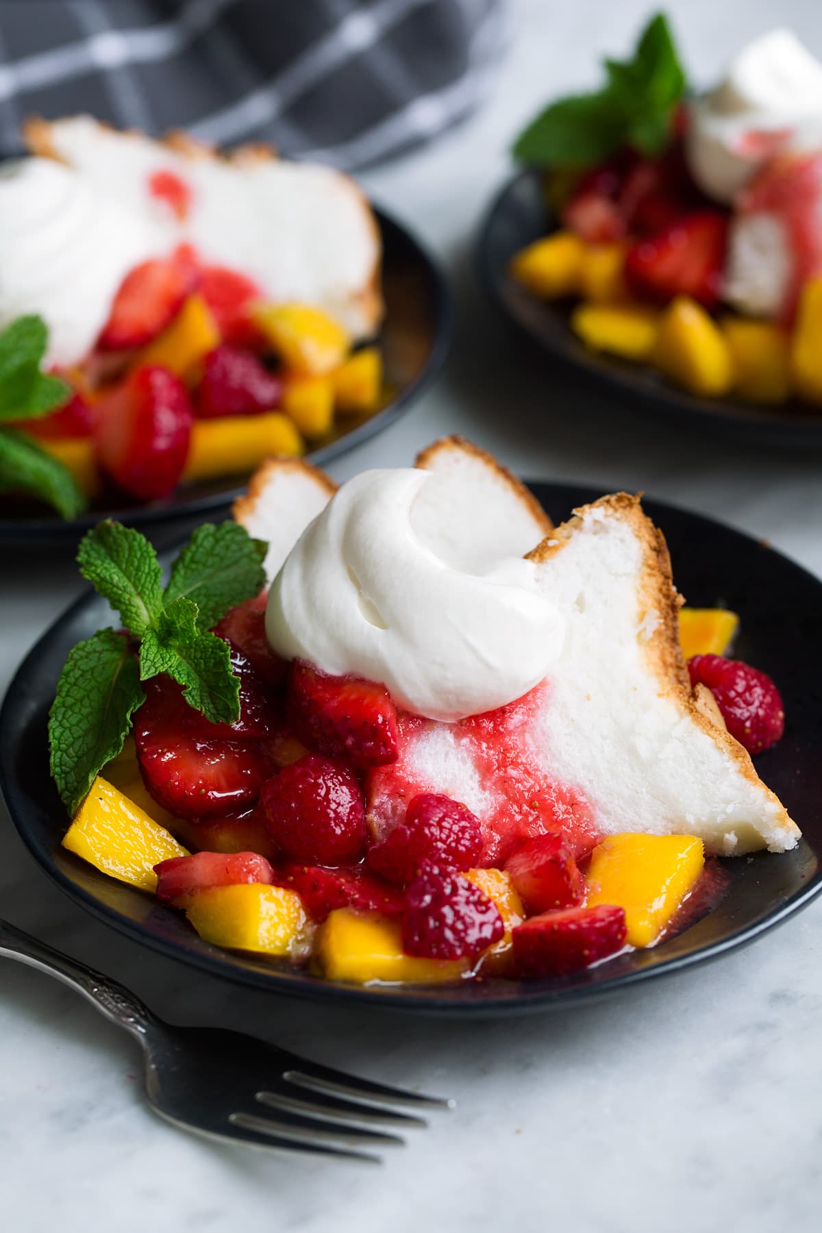 Homemade whipped cream served over angel food cake with a side of fruit on a black dessert plate.