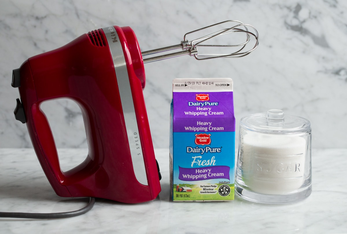 Whipped cream sugar and an electric hand mixer on a marble surface 