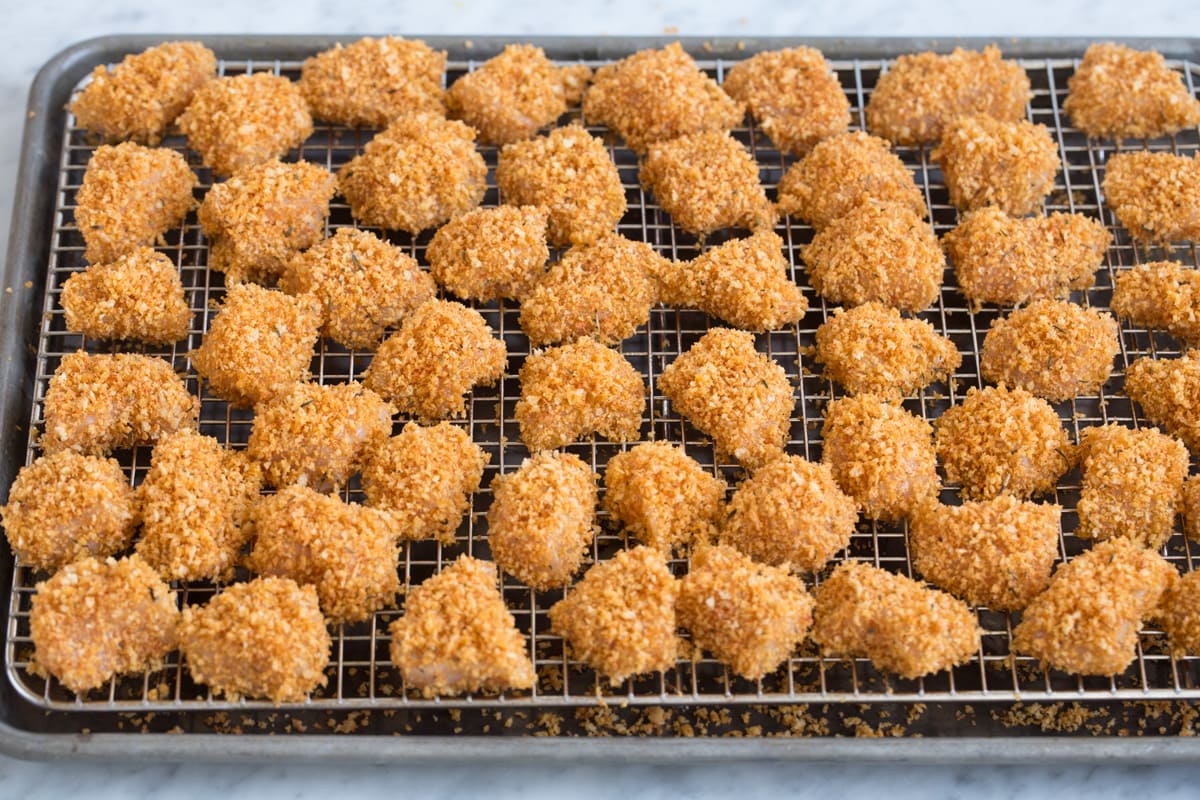 Showing how chicken nuggets look on wire rack over baking sheet before baking.