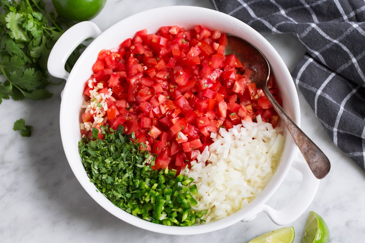 Pico de Gallo Showing how to make pico de gallo, mixing chopped tomato, onion, jalapeno, cilantro, garlic, lime and salt in a mixing bowl.