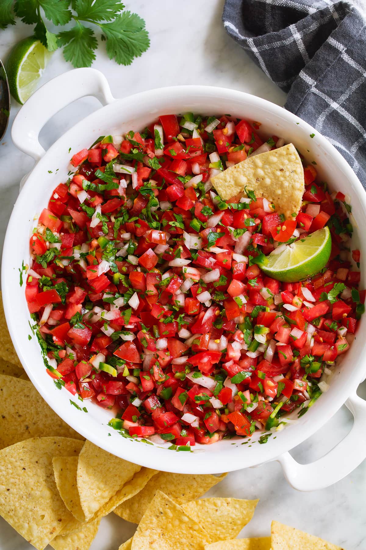 Overhead image of homemade pico de gallo in a white serving bowl with a side of tortilla chips.