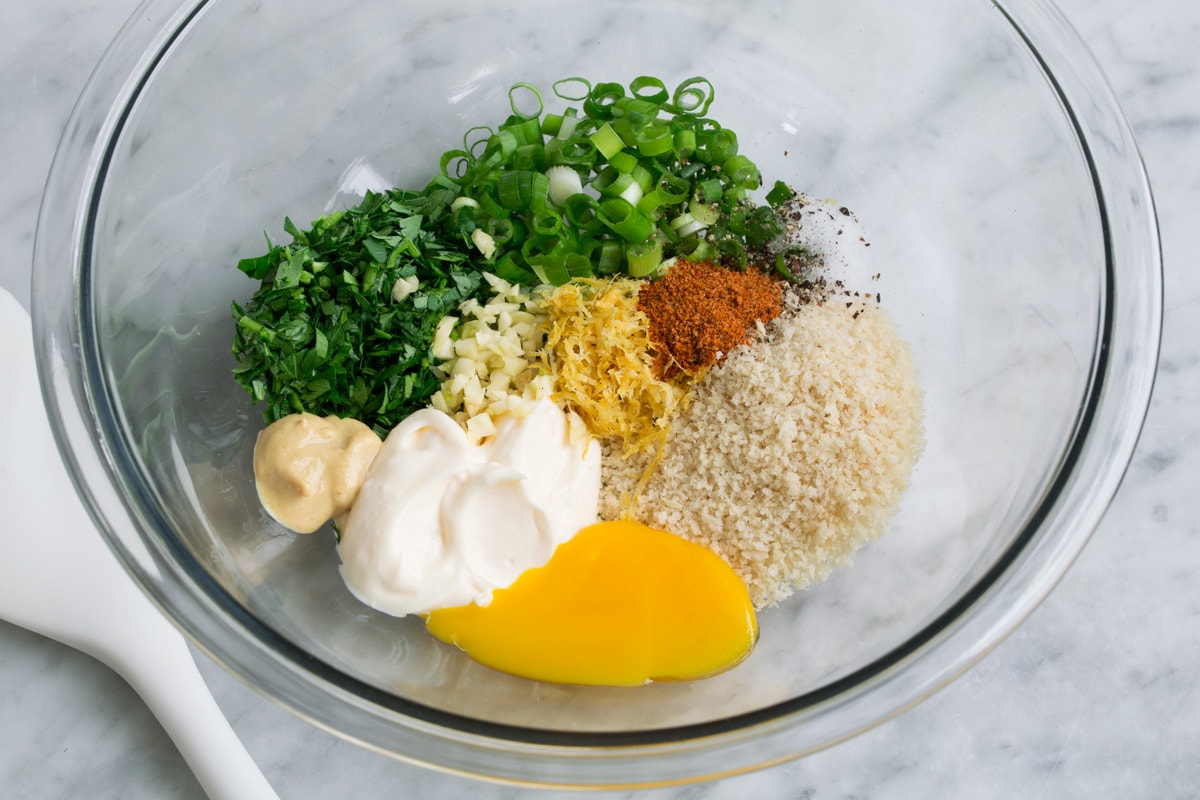 Showing how to make salmon patties, mixing bread crumbs, herbs, seasoning and mayonnaise in a glass mixing bowl.