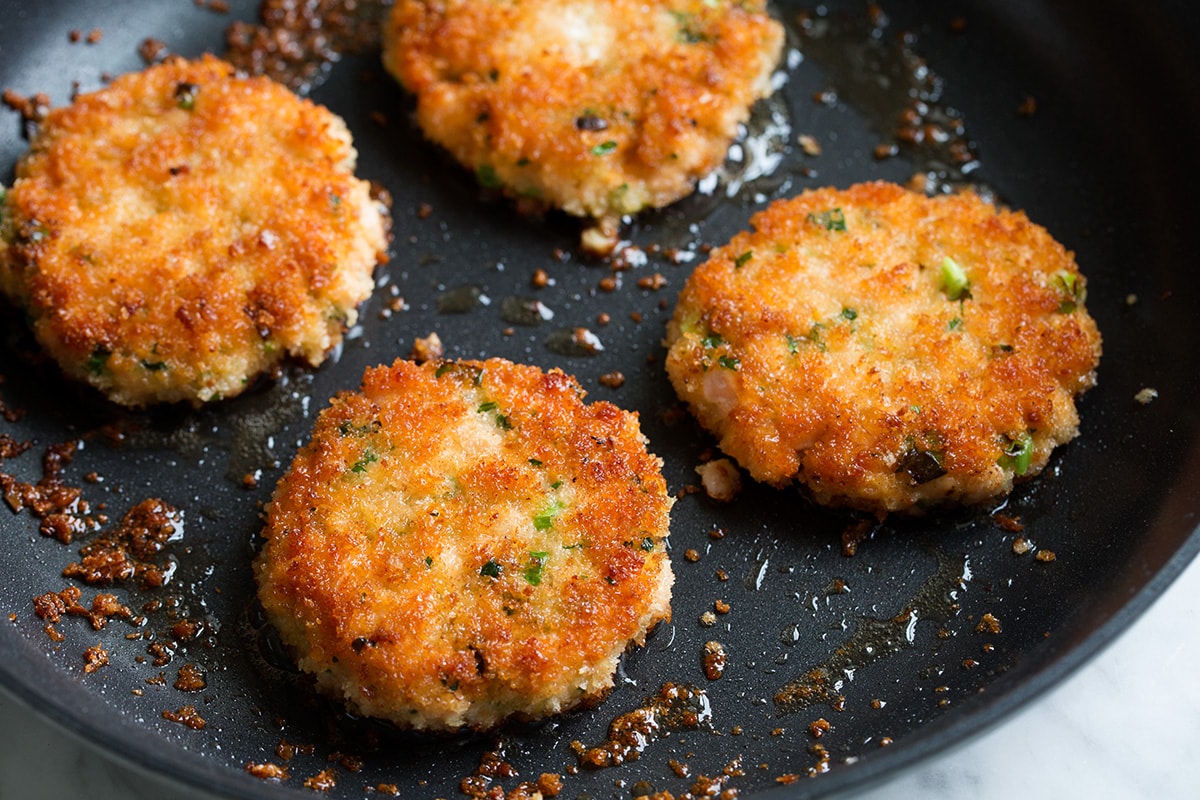 Salmon patties frying in oil in a skillet.