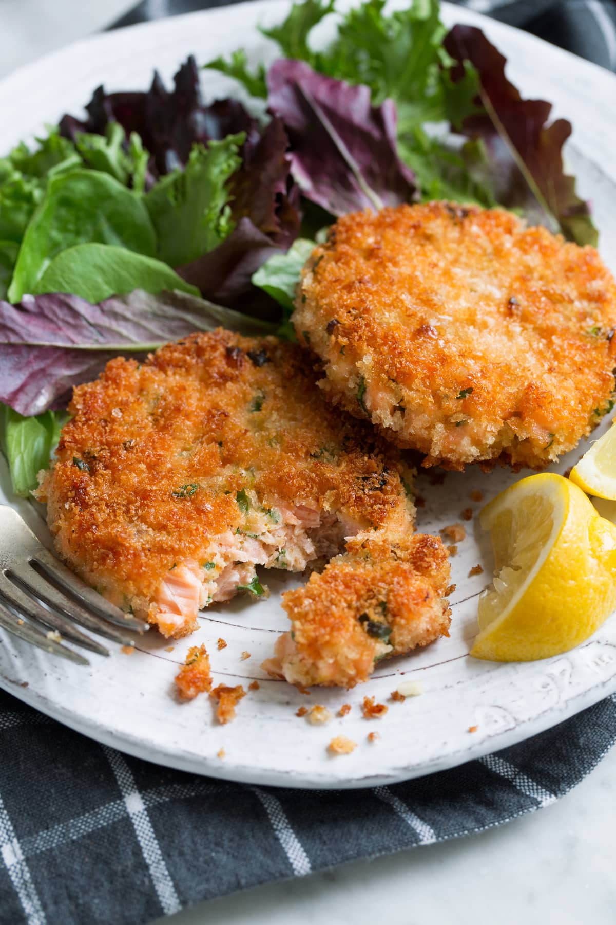Two salmon patties on a white serving plate with a side of salad.