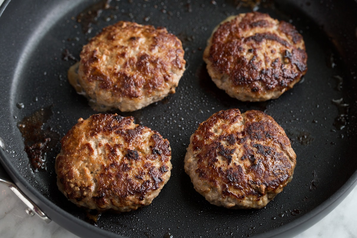 Four turkey burger patties in a large black skillet.