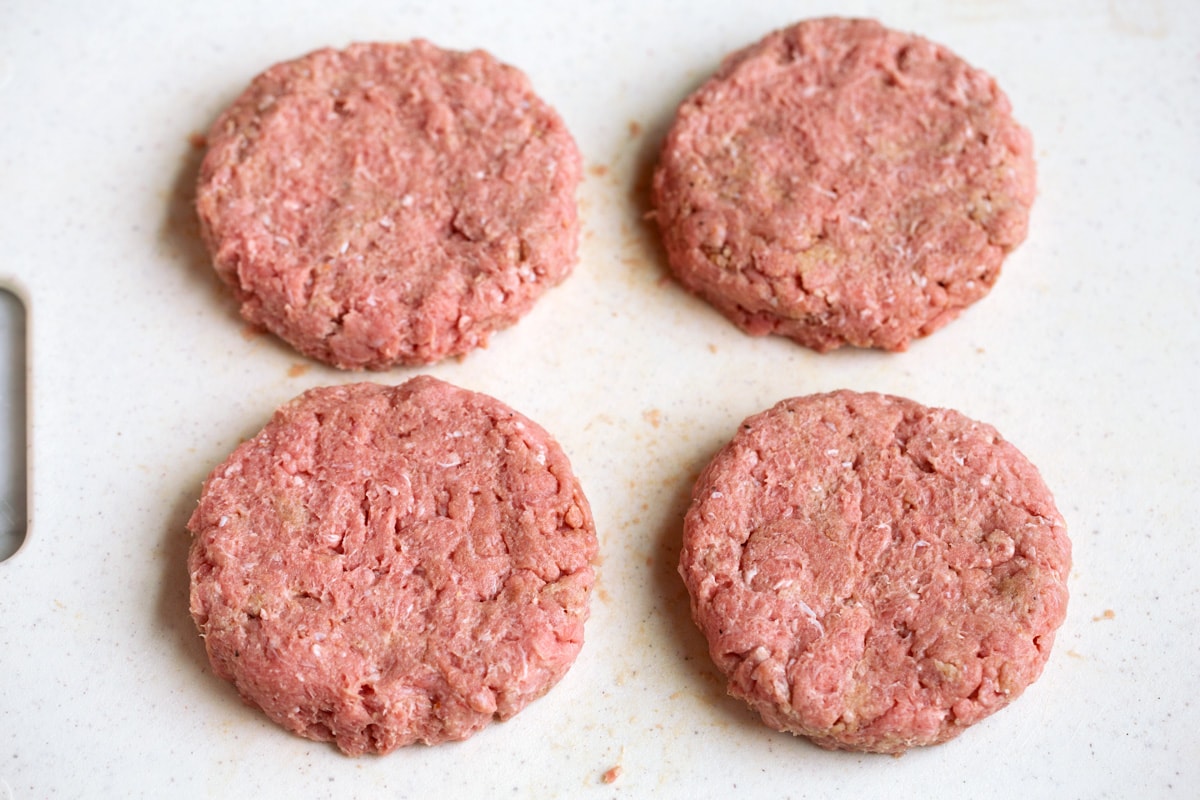 Four formed turkey burger patties on a cutting board.