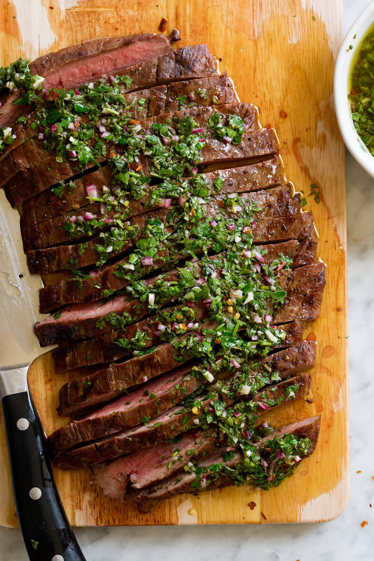 Showing a serving suggestion for homemade chimichurri, serving it over sliced steak.