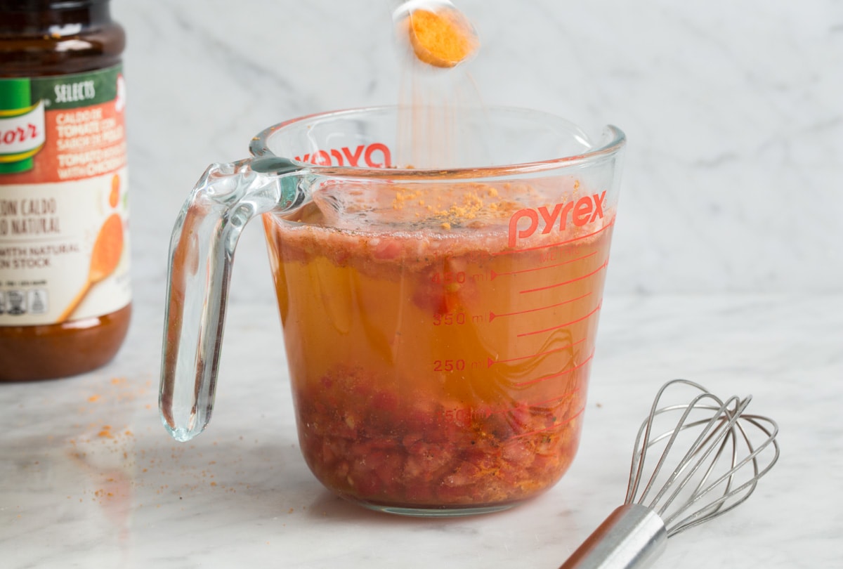 Showing how to make mexican rice. Mixing liquid ingredients and seasonings in a liquid measuring cup.