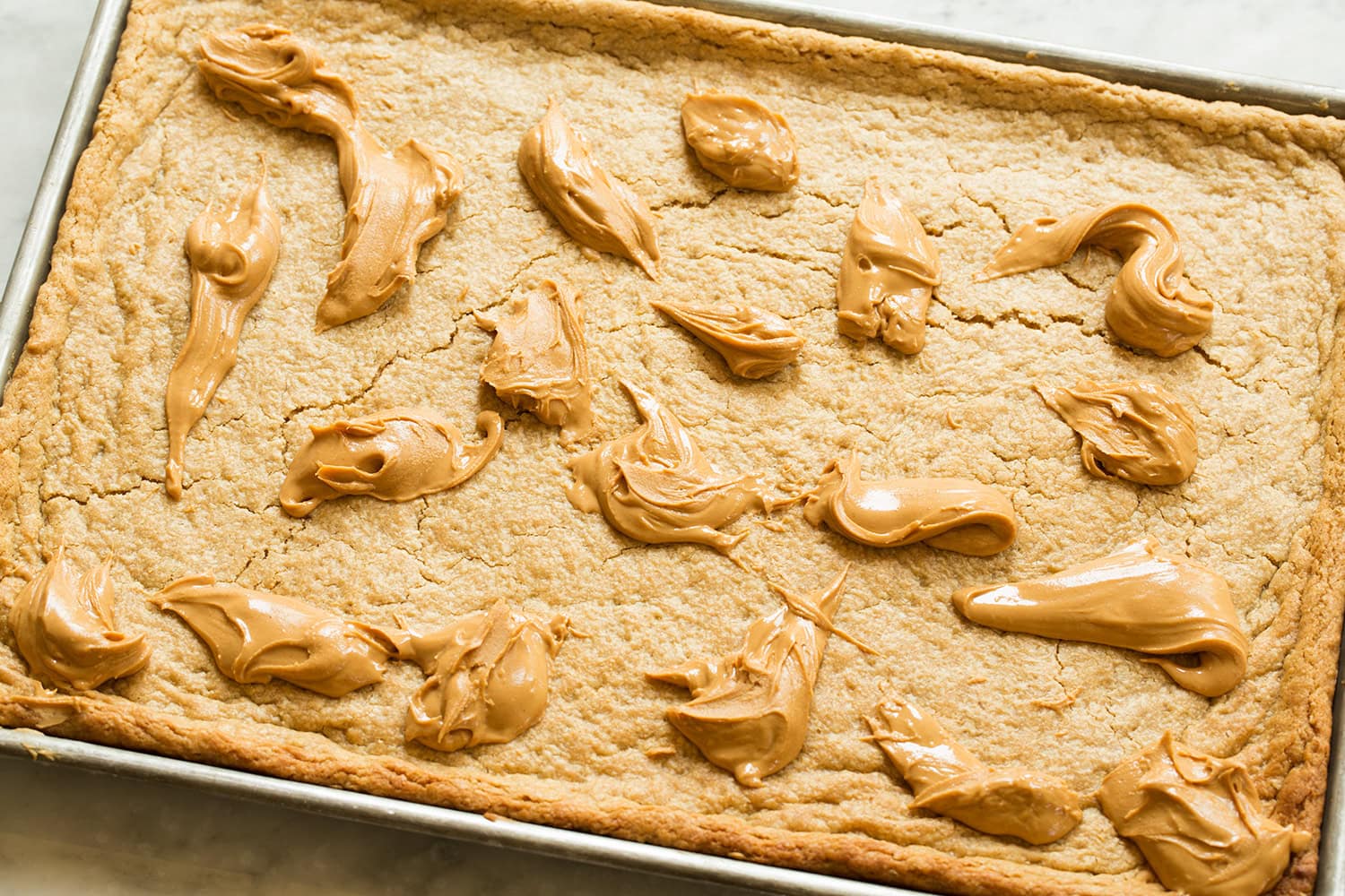 Spoonfuls of peanut butter spread over sheet of baked cookie bars.