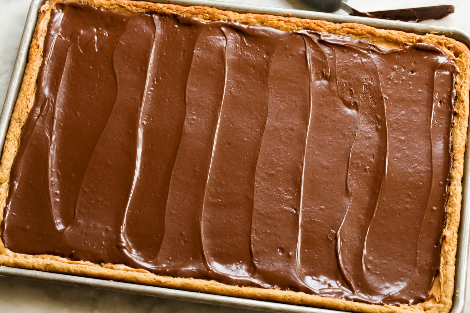 Chocolate frosting spread over layer of peanut butter.