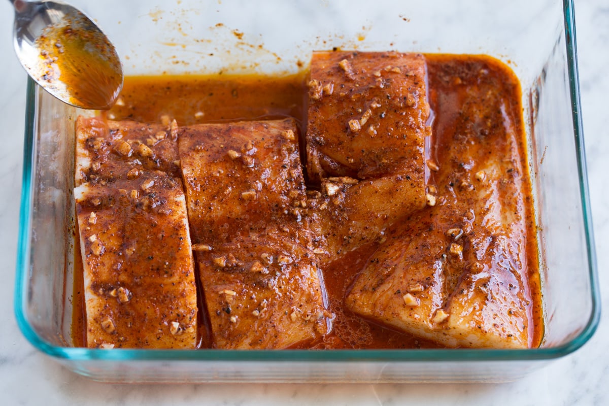 Spooning marinade over fish in baking dish.