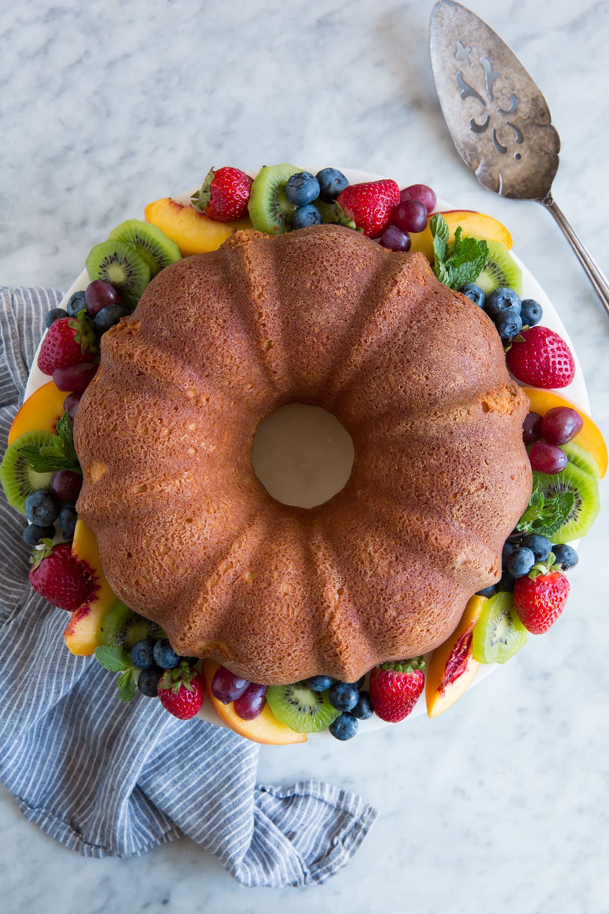Overhead image of whole pound cake on a cake stand with colorful fresh fruit around edges.