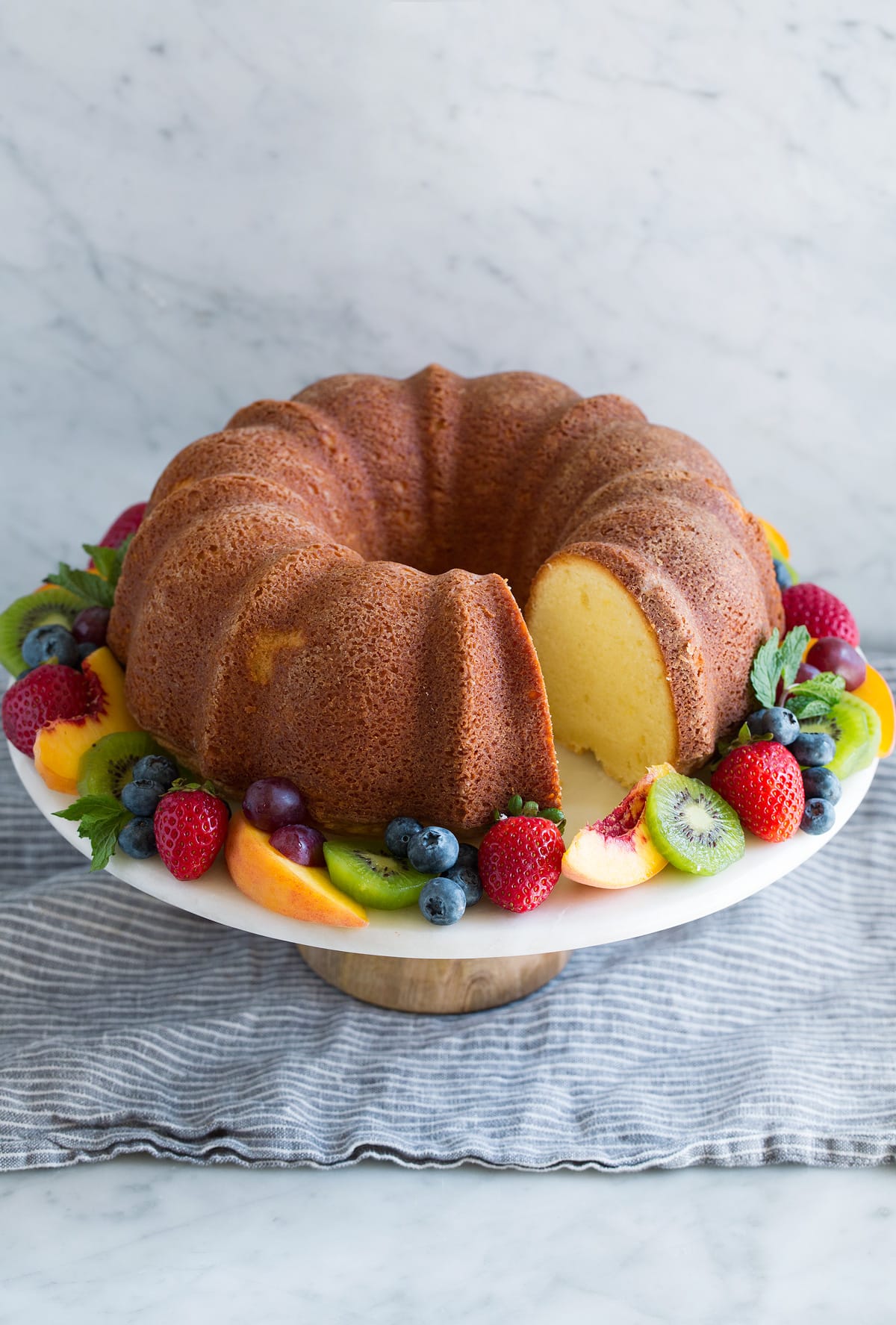 Pound cake with one sliced removed on a cake stand garnished with a ring of fresh fruit around the edges.