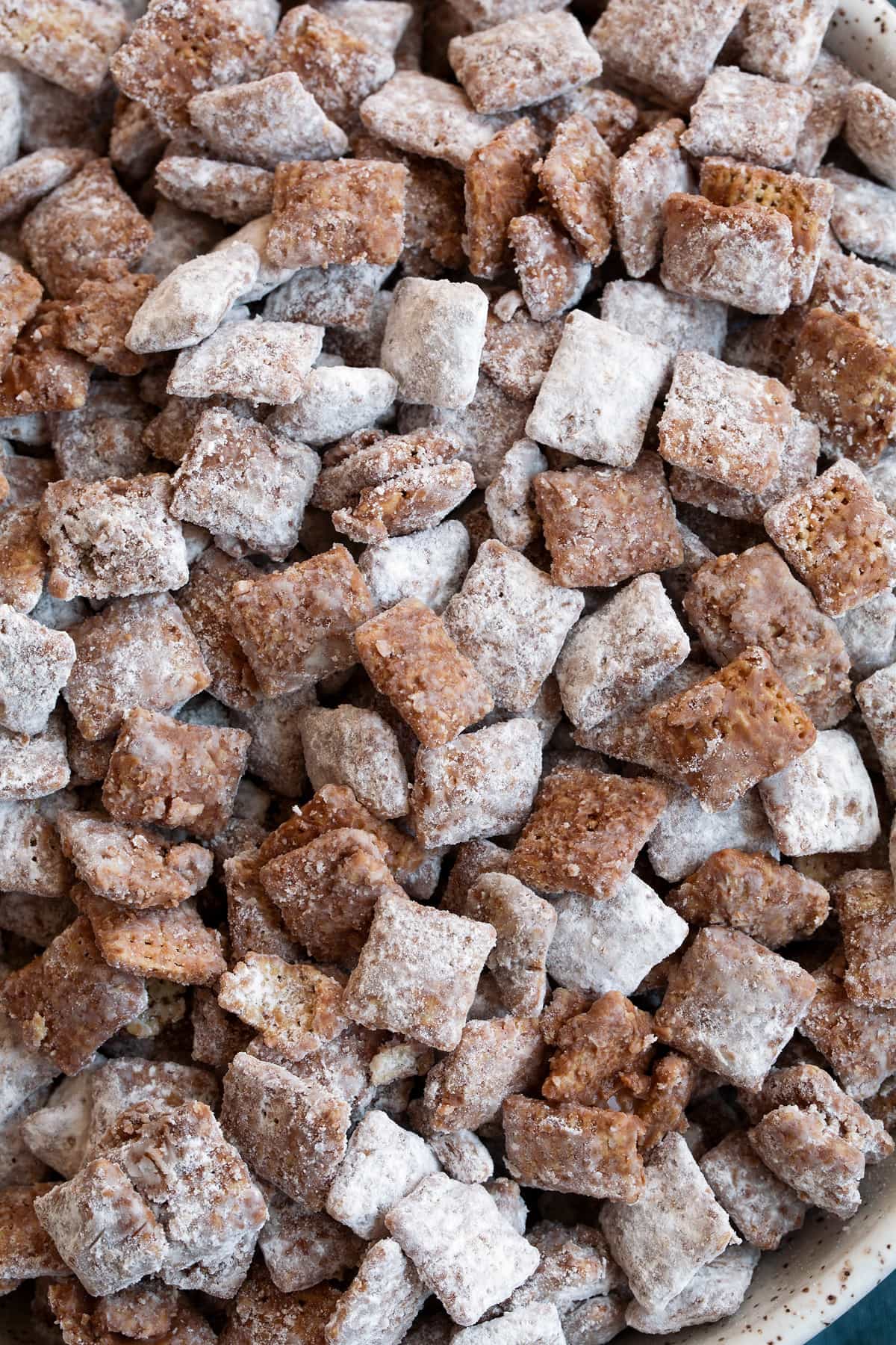 Perfect Puppy Chow {Muddy Buddies}! - one of my go-to treats! We love to take these on vacation, they're perfect for parties and holidays too! #muddybuddies #puppychow #treat #chocolate #chex #peanutbutter Close up image of muddy buddies showing texture of chocolate coating, powdered sugar and cereal.