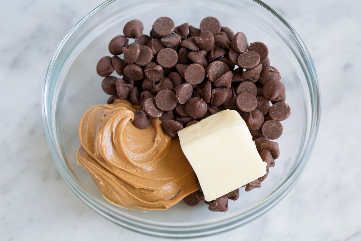 Perfect Puppy Chow {Muddy Buddies}! - one of my go-to treats! These are dangerously addictive! Perfect for parties, holidays and traveling too. #muddybuddies #puppychow #treat #chocolate #chex #peanutbutter Showing how to make muddy buddies. Adding chocolate chips, peanut butter and butter in a glass mixing bowl.