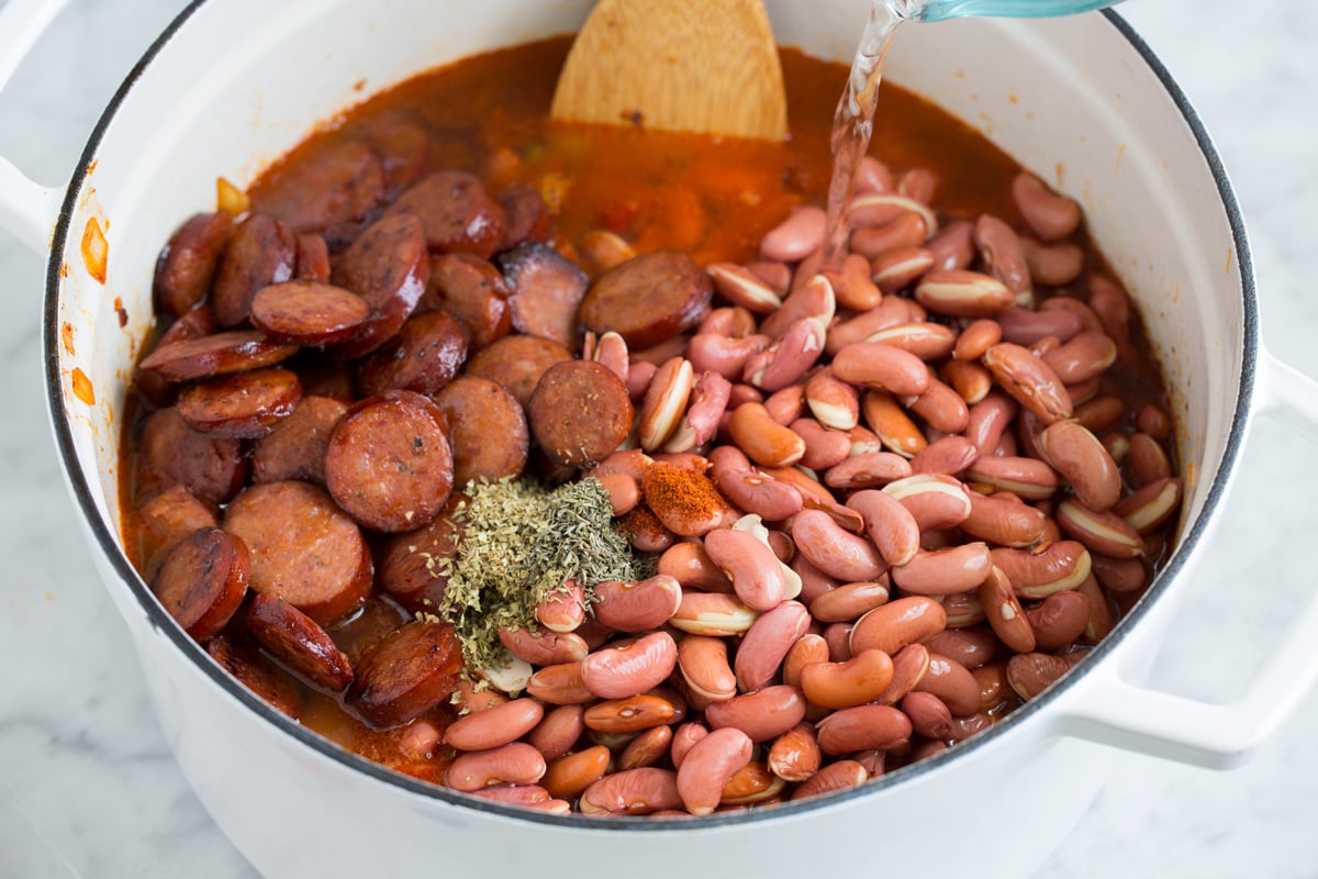 Adding soaked beans, sausage and water to pot of sauteed vegetables.