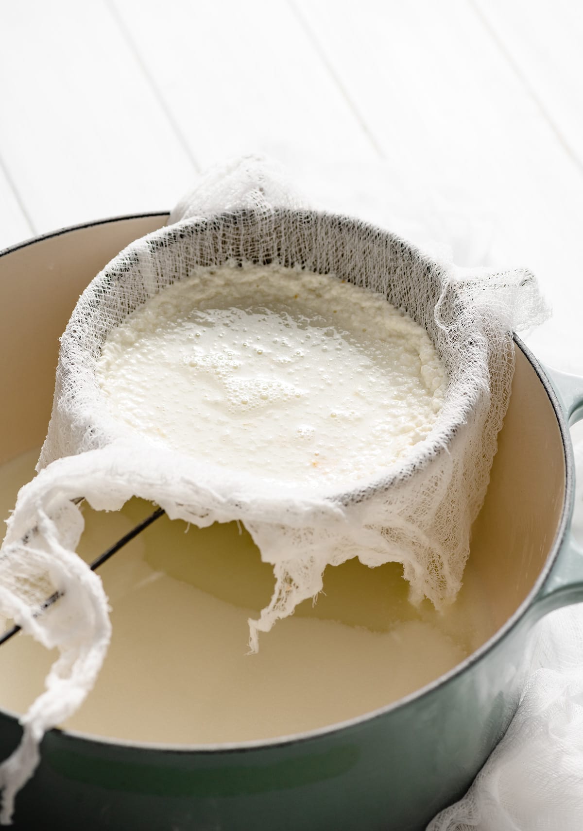 Ricotta cheese curds straining in a fine mesh sieve lined with cheese cloth. Sieve is resting over a large pot to drain.