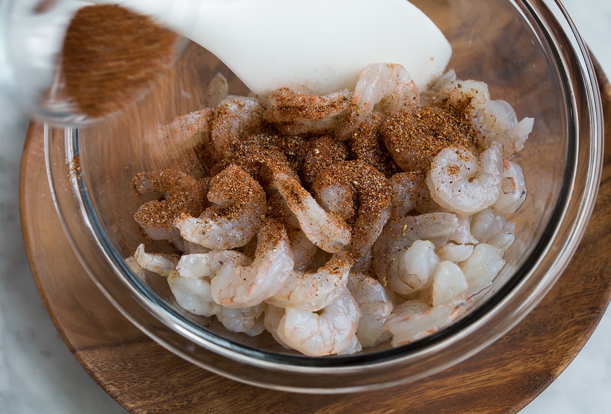 Showing how to make Shrimp Tacos. Tossing shrimp in a glass mixing bowl with taco seasonings.