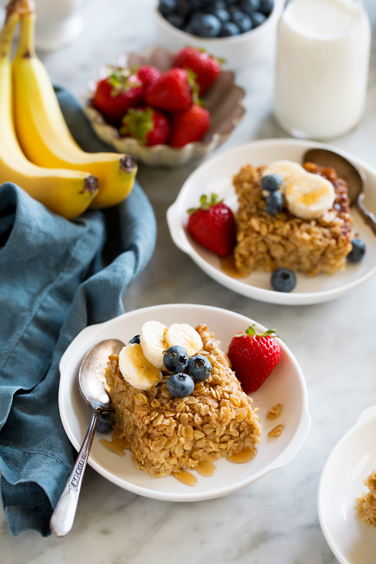Squares of baked oatmeal topped with fresh fruit in white serving bowls.