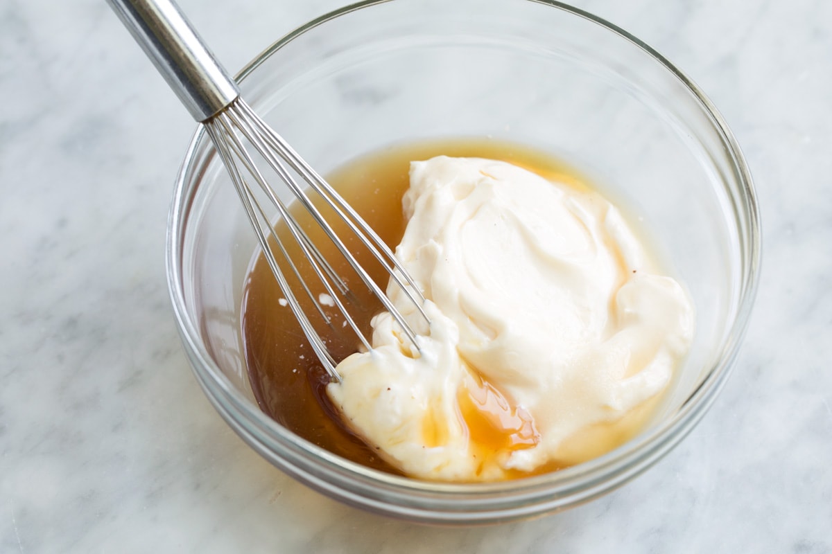 Mixing broccoli salad dressing ingredients in a glass mixing bowl.