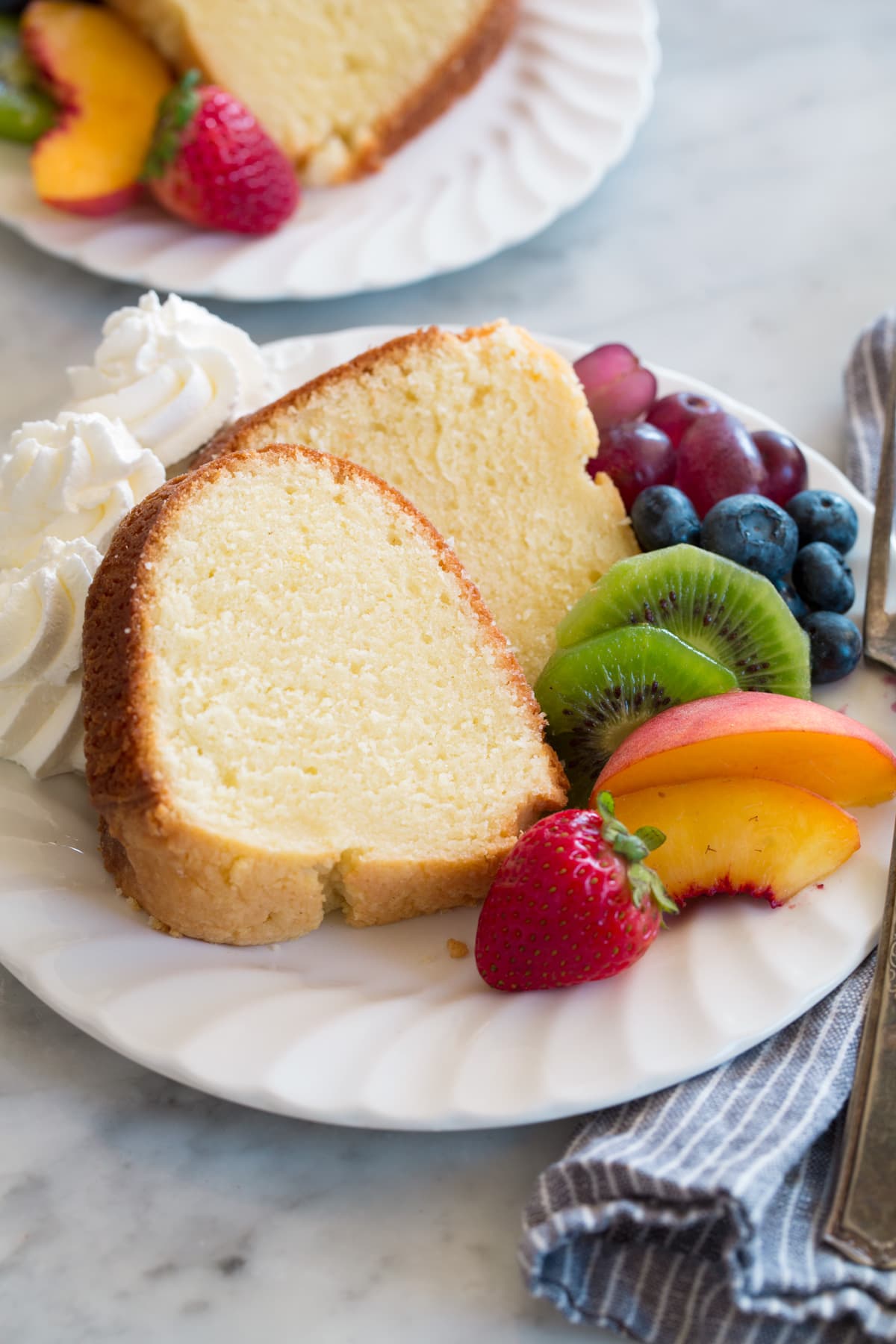 Slice of pound cake on a dessert plate with a side of fresh fruit and whipped cream.