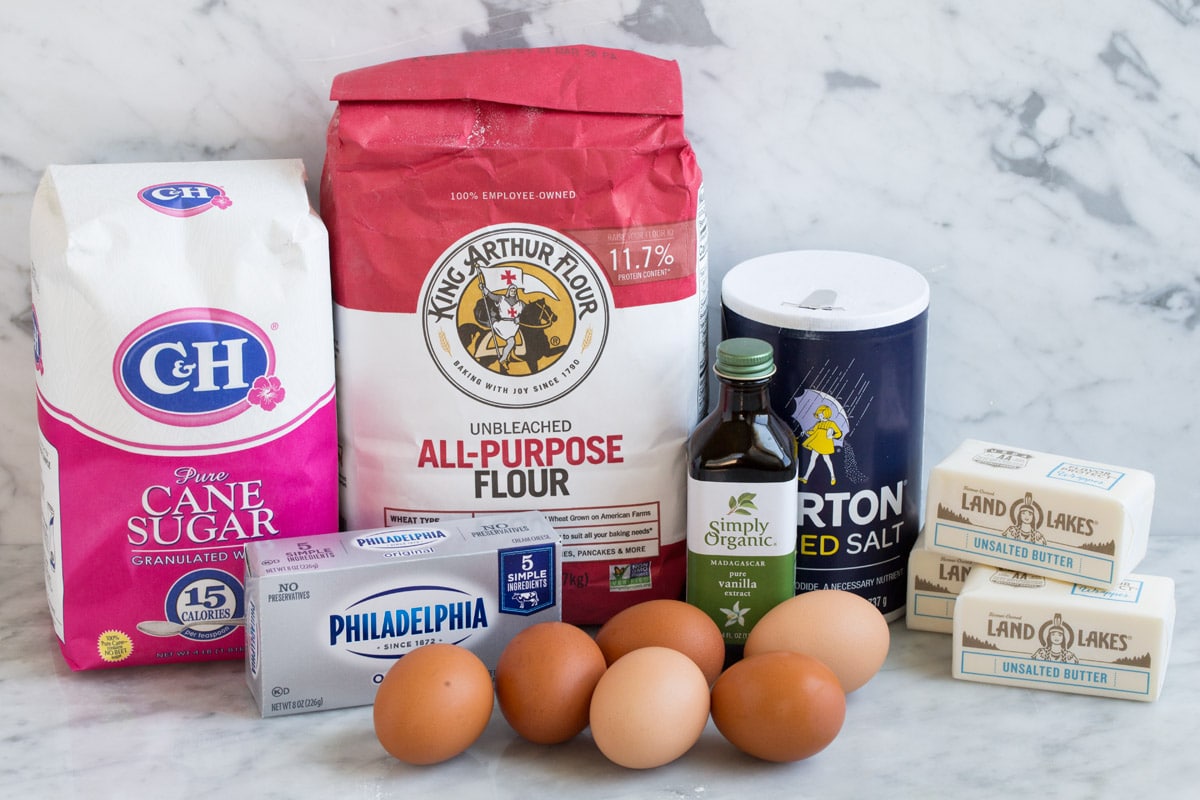 Ingredients to make pound cake shown here including flour, sugar, butter, cream cheese, eggs, salt and vanilla.