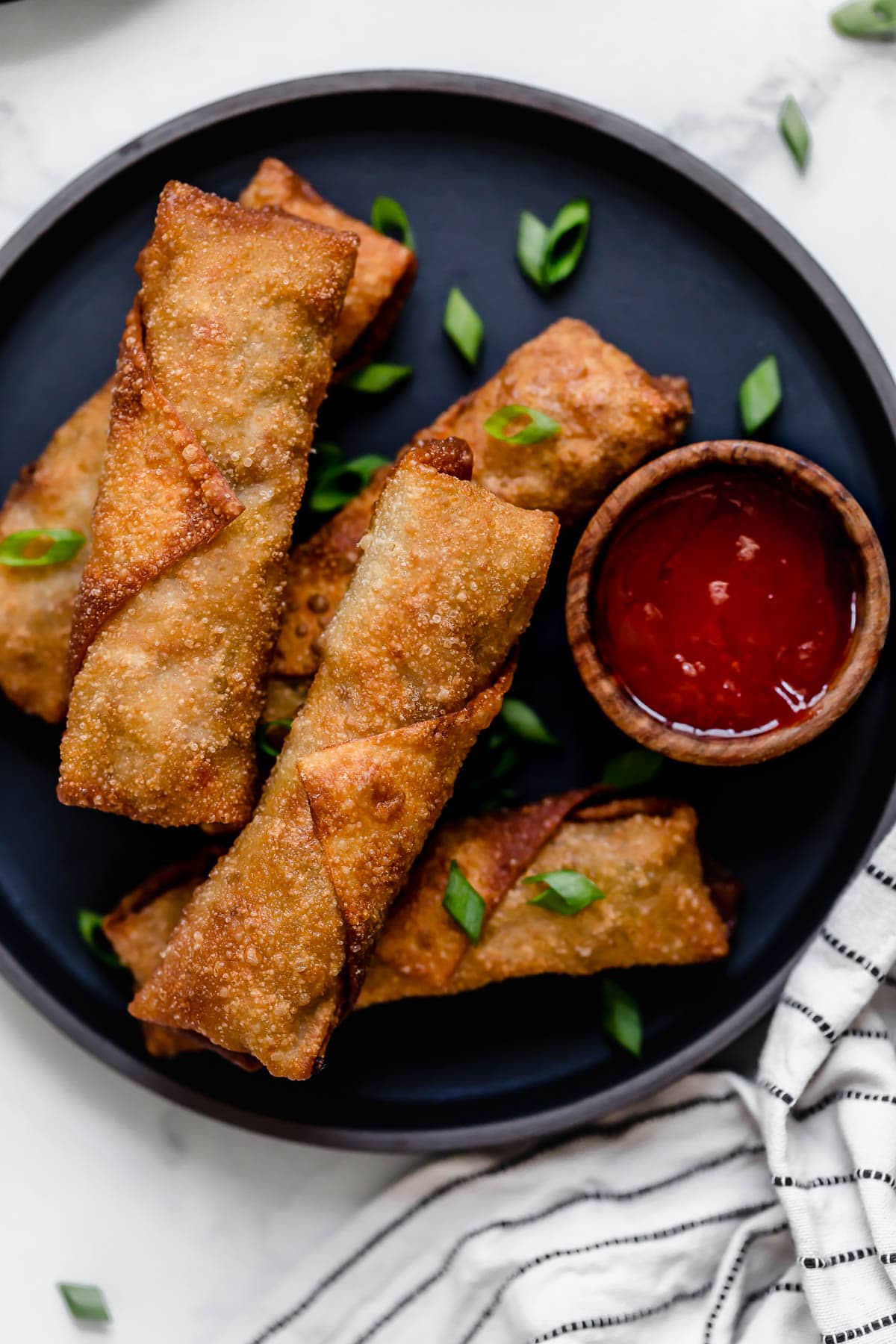 Egg Rolls {Fried or Baked} Five egg rolls on a dark plate with a side of dipping sauce.