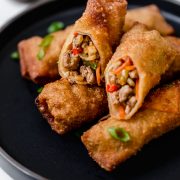 Egg rolls stacked on a black plate with one cut in half to show exterior.