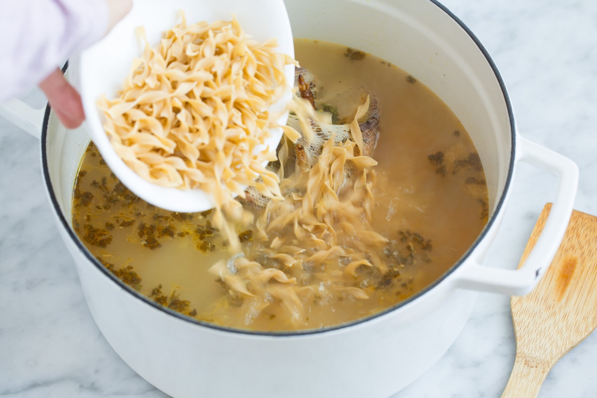 Adding egg noodles to broth mixture in pot.