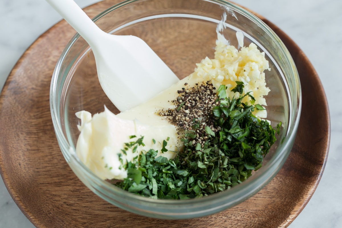 Garlic Bread Mixing butter, herbs and garlic in a glass mixing bowl.