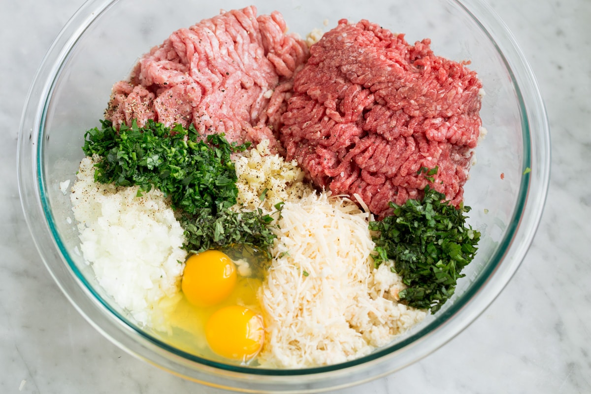 Ground beef, ground pork, fresh herbs, parmesan, eggs, onion, garlic and soaked breadcrumbs in a glass mixing bowl.