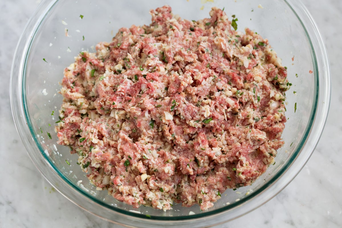 Mixed raw meatball mixture in a glass mixing bowl.