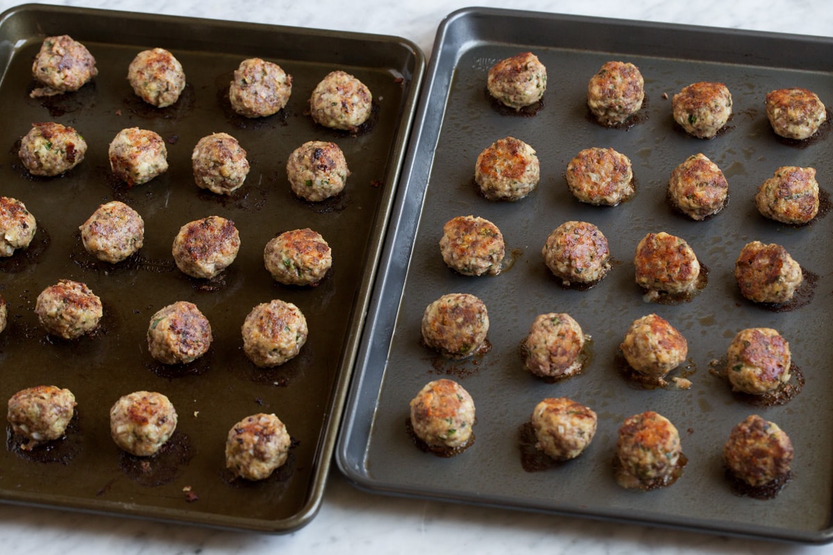 Cooked meatballs on two dark baking sheets.