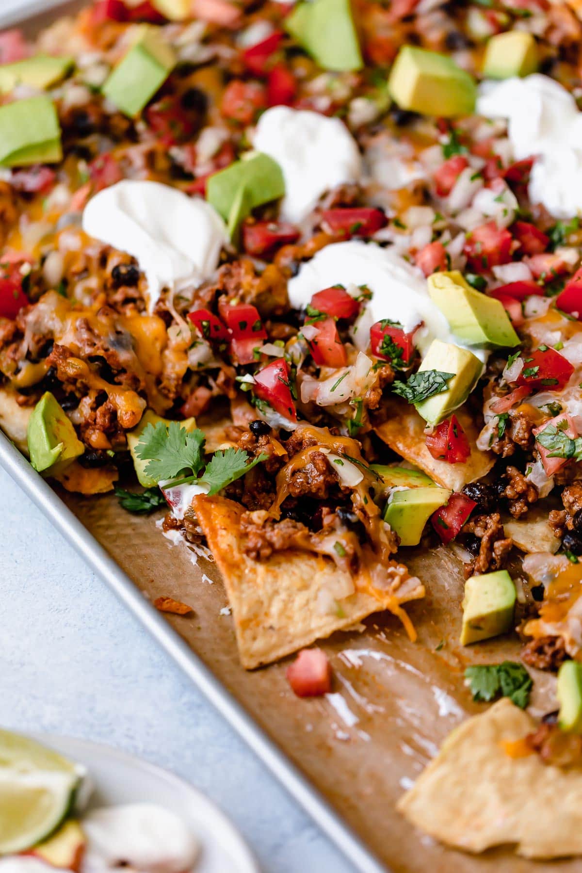 Easy Nachos - layered with seasoned beef and black beans, melty cheese, avocado and sour cream. SO GOOD! #nachos #sheetpan #beef #blackbeans #dinner #recipe Nachos on a baking sheet with beef, black beans, cheese, pico, and sour cream.