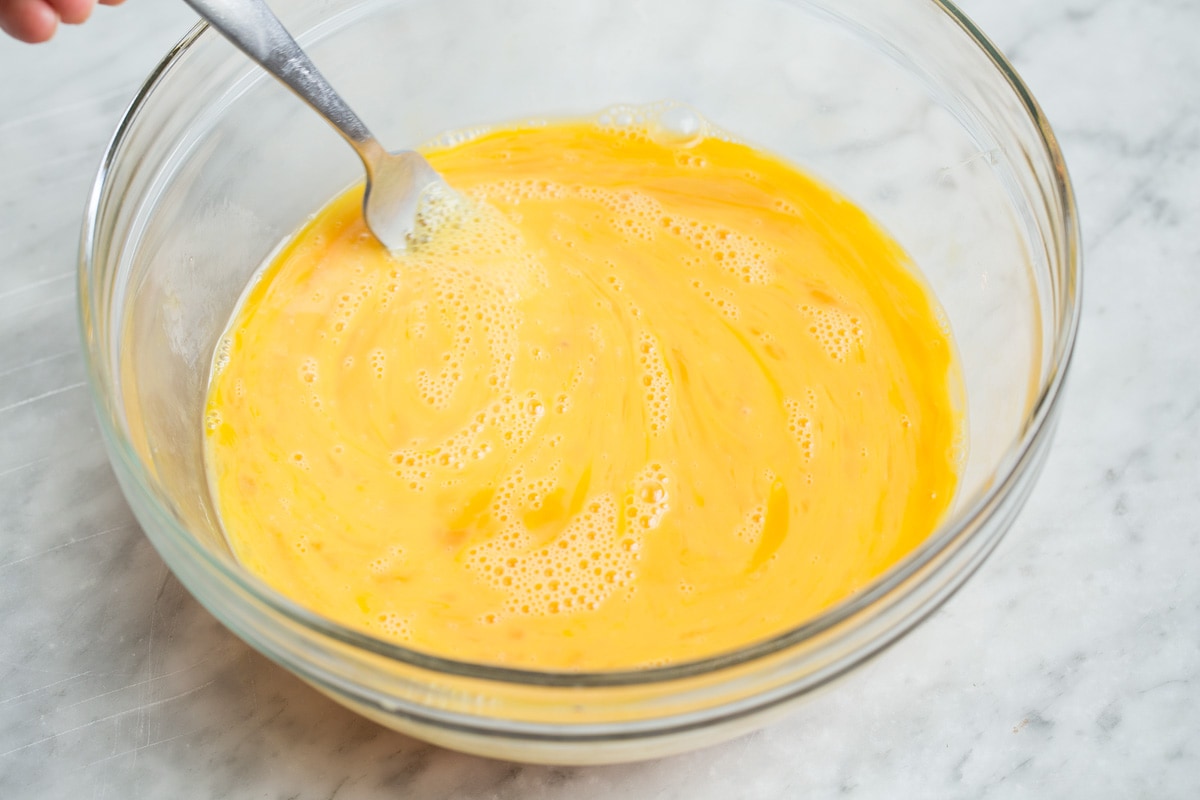 Whisking eggs with a fork in a glass bowl.