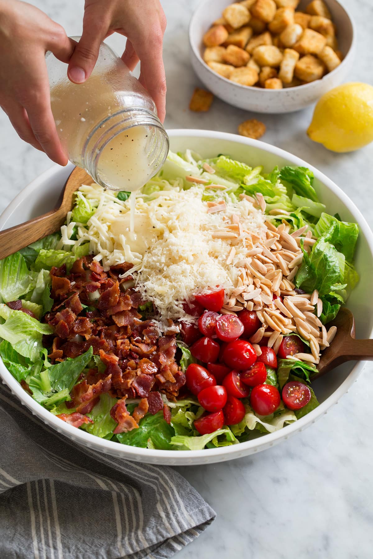 Pouring lemon dressing over Family Favorite salad in a large white bowl.